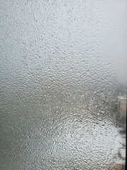 Texture of frozen glass window in heavy cold weather outdoors. Blurry iced droplets outside the window. Cold weather background with copy space. Shot through icy frost covered window