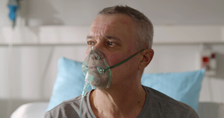 Portrait of elderly person with oxygen mask sitting up in hospital bed and looking around