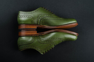 A pair of classic men's shoes of green color lies on a black background