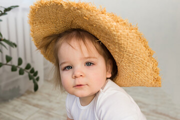 portrait of a little baby girl in a straw hat and white bodysuit on a white background with space for text