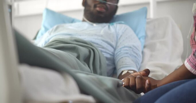 Cropped shot of african wife visiting husband in hospital holding hands and supporting