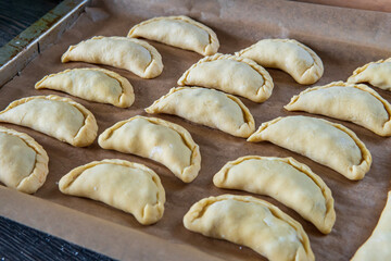 Uncooked empanadas on a baking tray. Traditional Latin American baked beef pastry ready for the oven. Gluten free savory appetizer with meat filling. Handmade typical dish in Spain or Argentina. Side