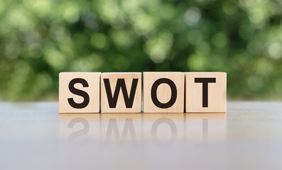 SWOT word written on wooden blocks. The text is written in black letters and is reflected in the mirror surface of the table. Business concept for your design.