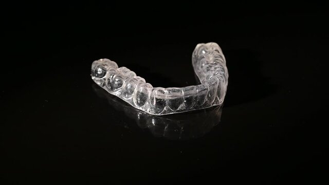 Removable plastic retainers for bite correction revolve against a black background