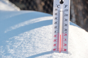 The thermometer lies on the snow and shows a negative temperature in cold weather on the blue...