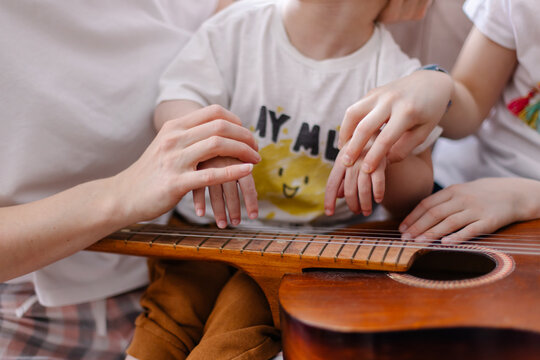 Hands of a child with cerebral palsy close-up. Music rehabilitation. Musical instrument guitar strings. Vibration sounds. Lessons with the disabled