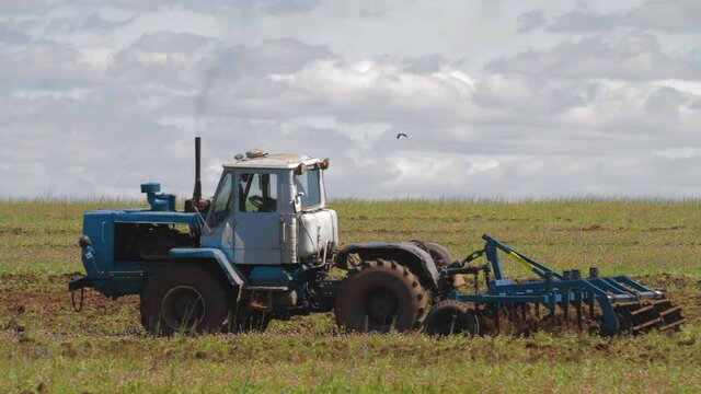 Tractor cuts furrows in farm field for sowing farm tractor with rotary harrow plow preparing land for sowing. Tractor with harrows prepares the agricultural land for planting crop