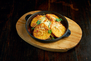 A traditional Ukrainian dish - potato pancakes with sour cream and cheese baked in the oven, served on a wooden board. Dark background. Tarditional draniki, deruny.