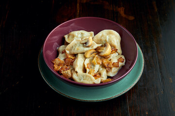 Traditional Ukrainian dumplings filled with mashed potato and fried onions, served in a red bowl on a black background. Close up view on Pierogi or varenyky