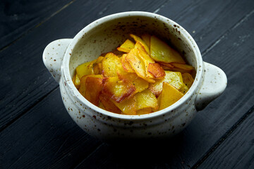 Appetizing side dish - fried potatoes with onions served in a white bowl on a dark background.