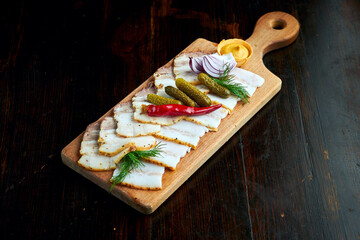 Assorted Ukrainian chopped bacon, Salo with pickled cucumber and mustard, served on a wooden board. Dark background. Traditional Slavic appetizer