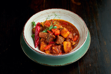 A traditional Hungarian dish is bograch or thick meat red goulash soup with potatoes and pork, served in a white bowl on a dark background. Transcarpathian cuisine