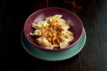 Traditional Ukrainian dumplings filled with cabbage and fried onions, served in a red bowl on a black background. Close up view on Pierogi or varenyky
