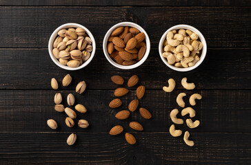Almonds with cashews and pistachios in white ceramic cups on a dark wooden background. Top view, concept, copy space, no people, flatlay