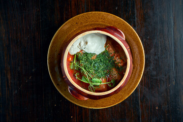 A traditional Ukrainian dish is stuffed cabbage rolls with minced meat and rice in a bowl with red sauce and sour cream. Black background