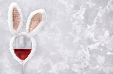Glass of rose or red wine with bunny ears on bright background. Easter decorations concept. Copy space for text.
