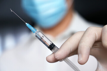 Syringe in doctor hand, man in medical mask and protective gloves preparing to injection. Concept of vaccination during covid-19 pandemic