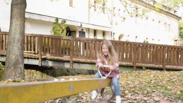 Cute little Caucasian girl laughs as she goes up and down on a seesaw - a restaurant in the background