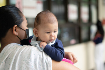 Asian Baby Girl looking down while being held by mother wearing a mask during pandemic