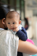 Vertical image of Asian Baby Girl Resting on mother's shoulders while being held by mother wearing a mask during pandemic