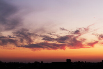 Dark, clear silhouettes of the roofs of houses with chimneys and pipes in the rays of the setting sun. Sunset in the city. Silhouette City landscape in the backlight of the sunset.