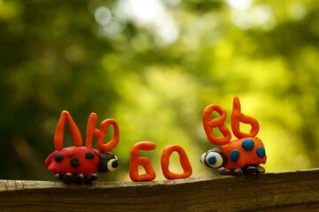 The inscription love in the Russian language. Next to it are two figures of ladybirds made of plasticine.