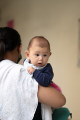 Vertical Shot Asian Baby Girl Opening and Closing her moth as she makes noise while being held by mother wearing a mask during pandemic