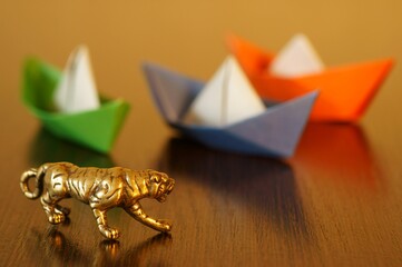A metal tiger and a group of colorful paper boats on the table. Business concept.
