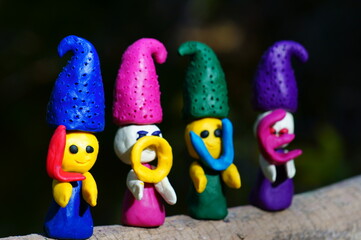 Figures of four fairy-tale dwarfs made of plasticine in the forest on a colored background. The elves have letters in their hands. The inscription love.