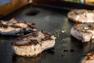 Marinated boneless pork chops cooking on a hibachi style outdoor large griddle