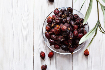 Dried rose hip berries in a glass plate on a white wooden table. Concept of traditional medicine.Organic rose hip - Antioxidant, source of vitamin C, immunity protection. Superfoods.
