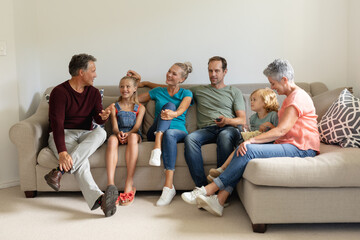 Fototapeta premium Senior caucasian man sitting on couch talking with his smiling three generation family