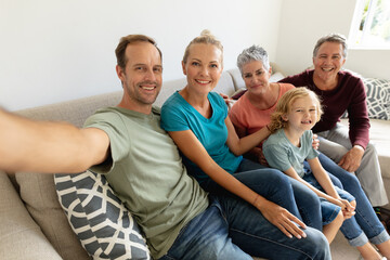 Caucasian father sitting on couch taking selfie with his wife, parents and son smiling and