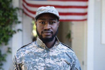 Portrait of african american male soldier standing in front of american flag outside home