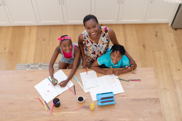 Fototapeta na wymiar Portrait of smiling african american mother sitting at table with son and daughter doing school work