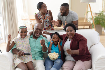 Excited african american parents, grandparents and grandchildren on couch watching tv and cheering