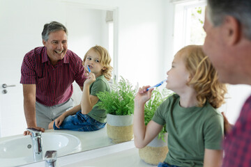 Smiling caucasian grandfather in bathroom with grandson brushing teeth both looking in mirror
