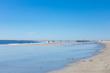 Flat, sandy shoreline with wide tide pools reflecting a bright blue sky, distant beachcombers, Tybee Island Georgia, horizontal aspect