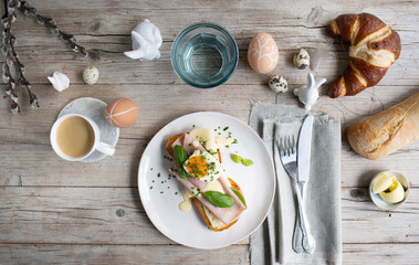 Easter breakfast with golden toasted Easter bread with butter and cheese and ham with egg and chives and basil with Easter decoration on light wooden background and various pastries