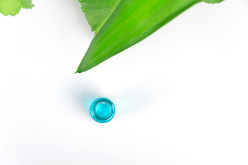 Obraz premium Top view of green plant leaves and a turquoise bottle of serum or oil on a white background with copy space. Flat lay. Concept of cosmetology, medicine