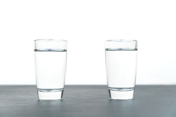 Close-up of two standing vodka glasses on a black table on a white background with copy space