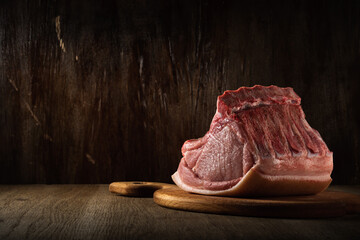 a whole freshly cut piece of raw pork loin lies on a cutting board on a brown wooden background. side view. artistic moody photo in simple rustic style with copy space