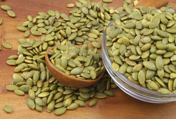 Pumpkin seeds in wooden spoon and glass bowl on wooden table