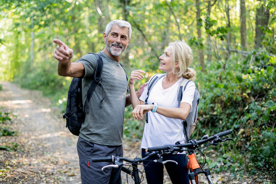 Smiling mature couple checking direction on smart watch in forest