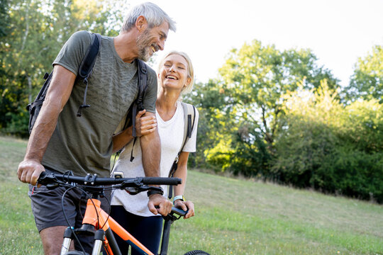 Smiling mature couple with bicycle standing in forest