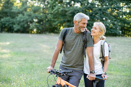 Smiling mature couple with bicycle looking at each other in forest