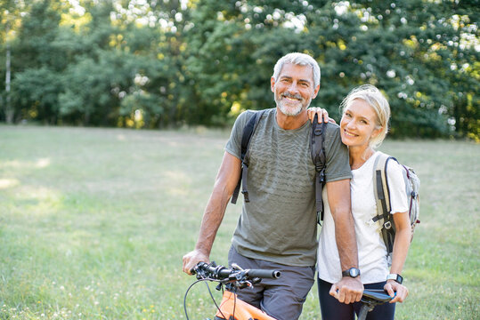 Portrait of smiling mature couple with bicycle standing in forest
