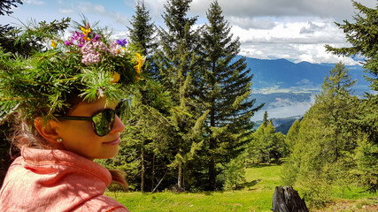 A woman in orange hoodie wearing a floral crown made of wild flowers and larch branches. Lush green...