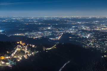 North Italy at night. Aerial view of the Sacro Monte di Varese (UNESCO site) with Varese on the right and the city of Milan on the horizon. View of the Po Valley (Pianura Padana) illuminated at dusk