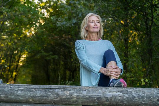 Smiling mature woman stretching her leg in forest